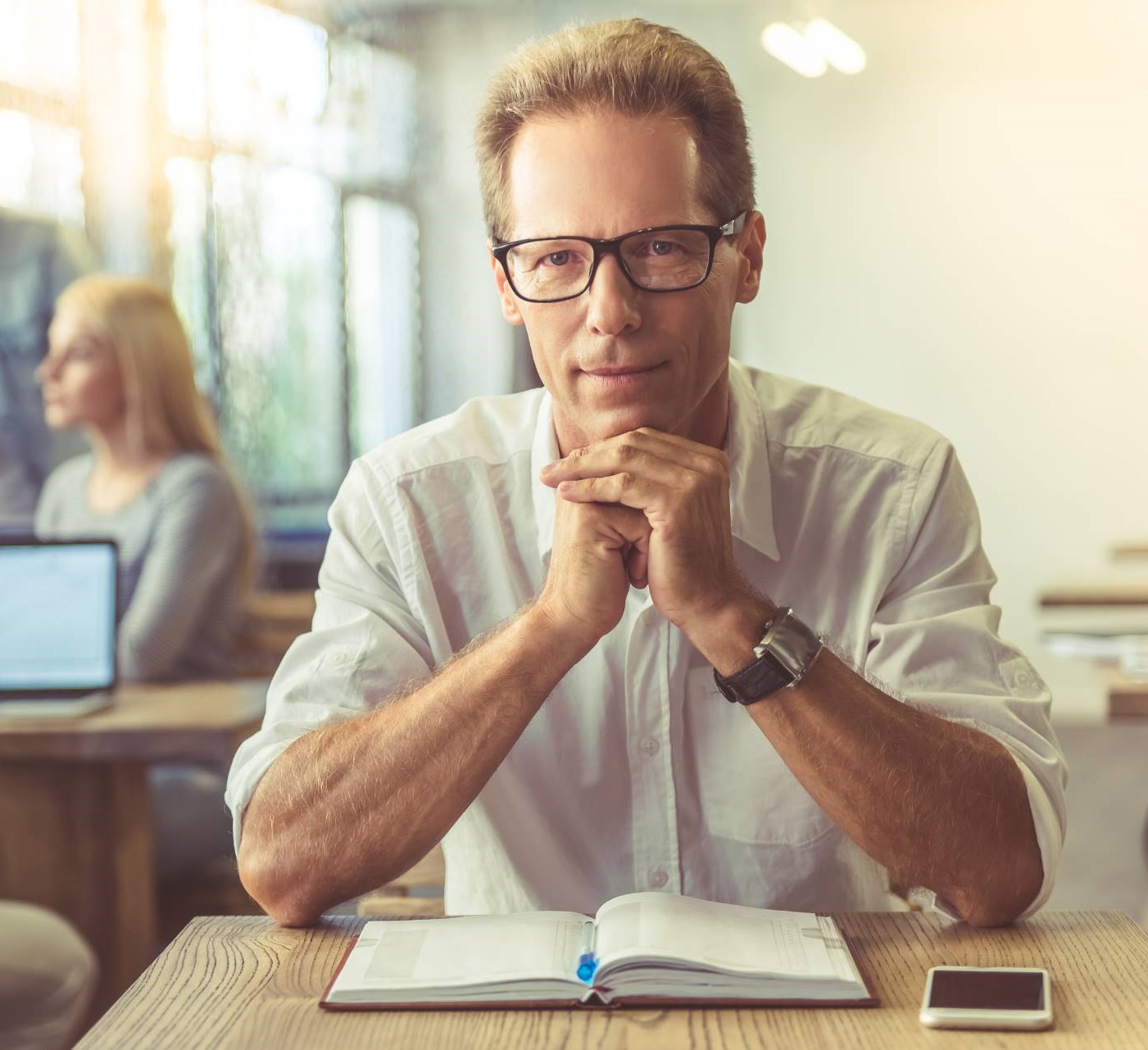 Businessman in shirt and eyeglasses is looking at camera.